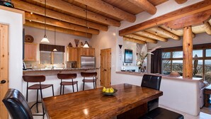 Un vaste espace dédié à la salle à manger, avec une table et des chaises en bois, une cuisine à l’arrière-plan et une vue sur l’extérieur grâce à de grandes fenêtres.