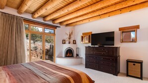 Une chambre dotée d’un grand lit, de poutres apparentes en bois au plafond, d’une cheminée, d’un téléviseur et offrant une vue sur l’extérieur.