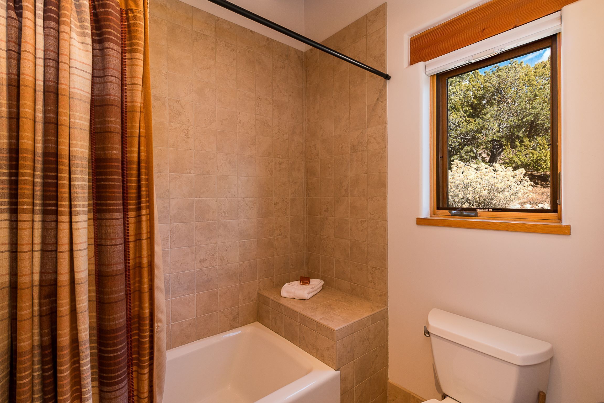 Une salle de bain avec une baignoire, des toilettes et une fenêtre donnant sur les arbres.