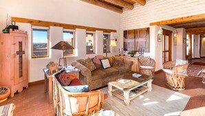Ein gemütliches Wohnzimmer mit Holzbalkendecke, einem braunen Sofa, einem Couchtisch und Korbstühlen.