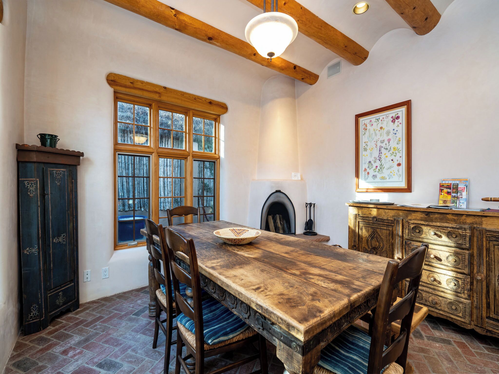 A rustic dining room with a wooden table and chairs, a fireplace, and a large window with multiple panes.