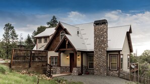 A rustic cabin with a stone chimney, wooden porch, and a gravel driveway. - Casa Oso Grande by Ruidoso Vacation Rentals (Ruidoso)