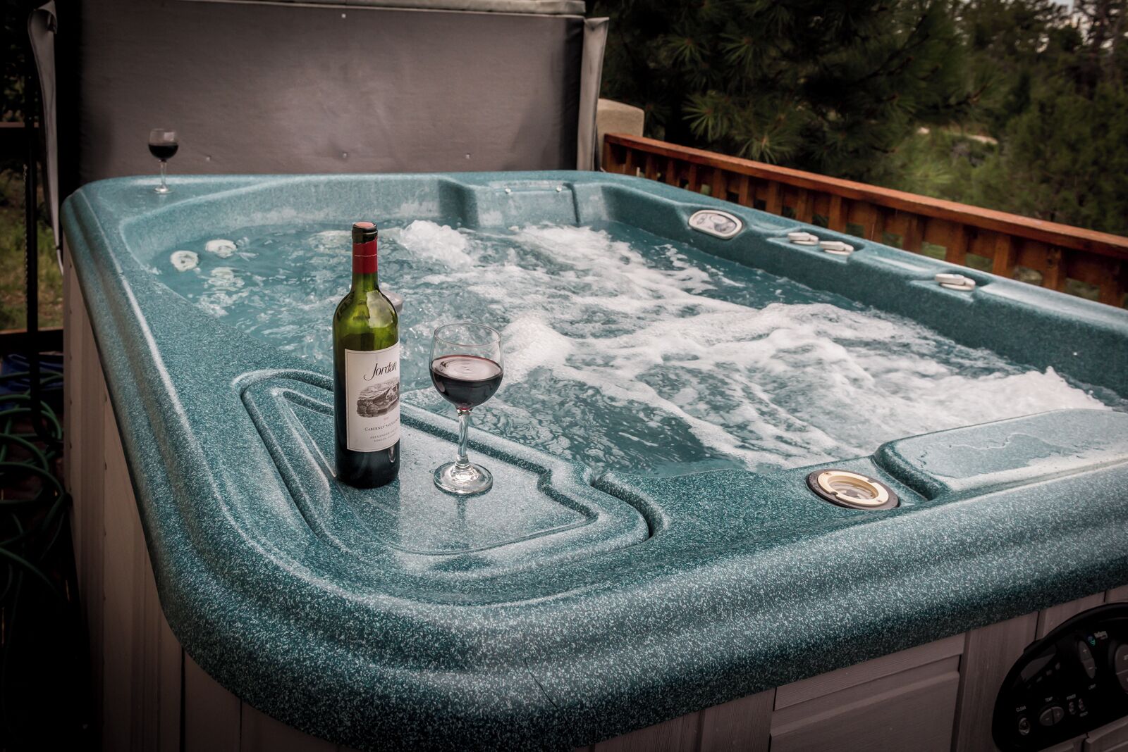 Una bañera de hidromasaje con superficie texturizada, una botella de vino y una copa de vino encima.