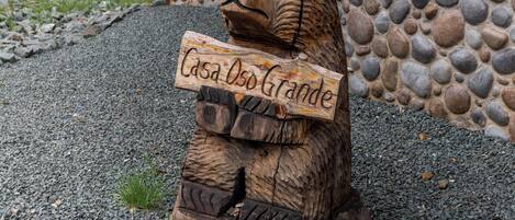 A wooden bear sculpture holding a sign that reads "Casa Usando Grande".