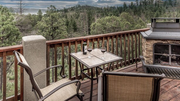 A deck with a stone fireplace, a table with two wine glasses, and a chair. - Casa Oso Grande by Ruidoso Vacation Rentals (Ruidoso)
