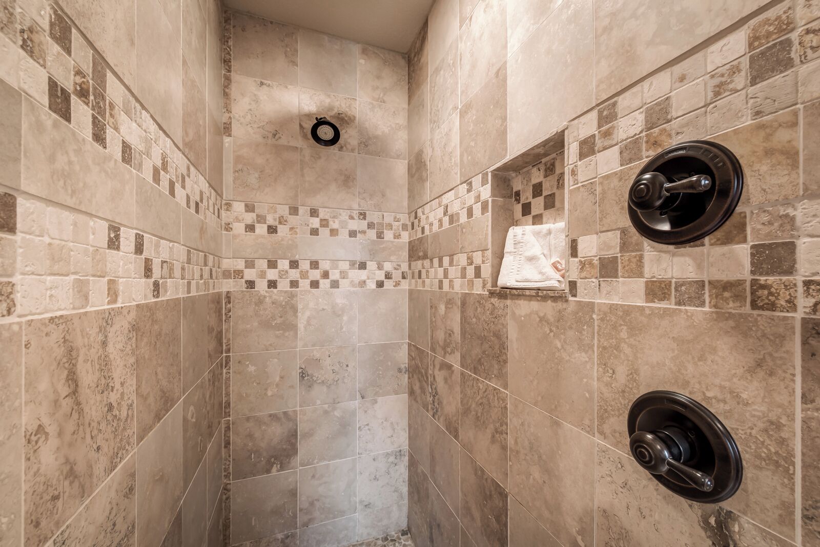 Een douche met beige tegels, een geruit patroon aan de onderkant, en twee zwarte douchesleutels.