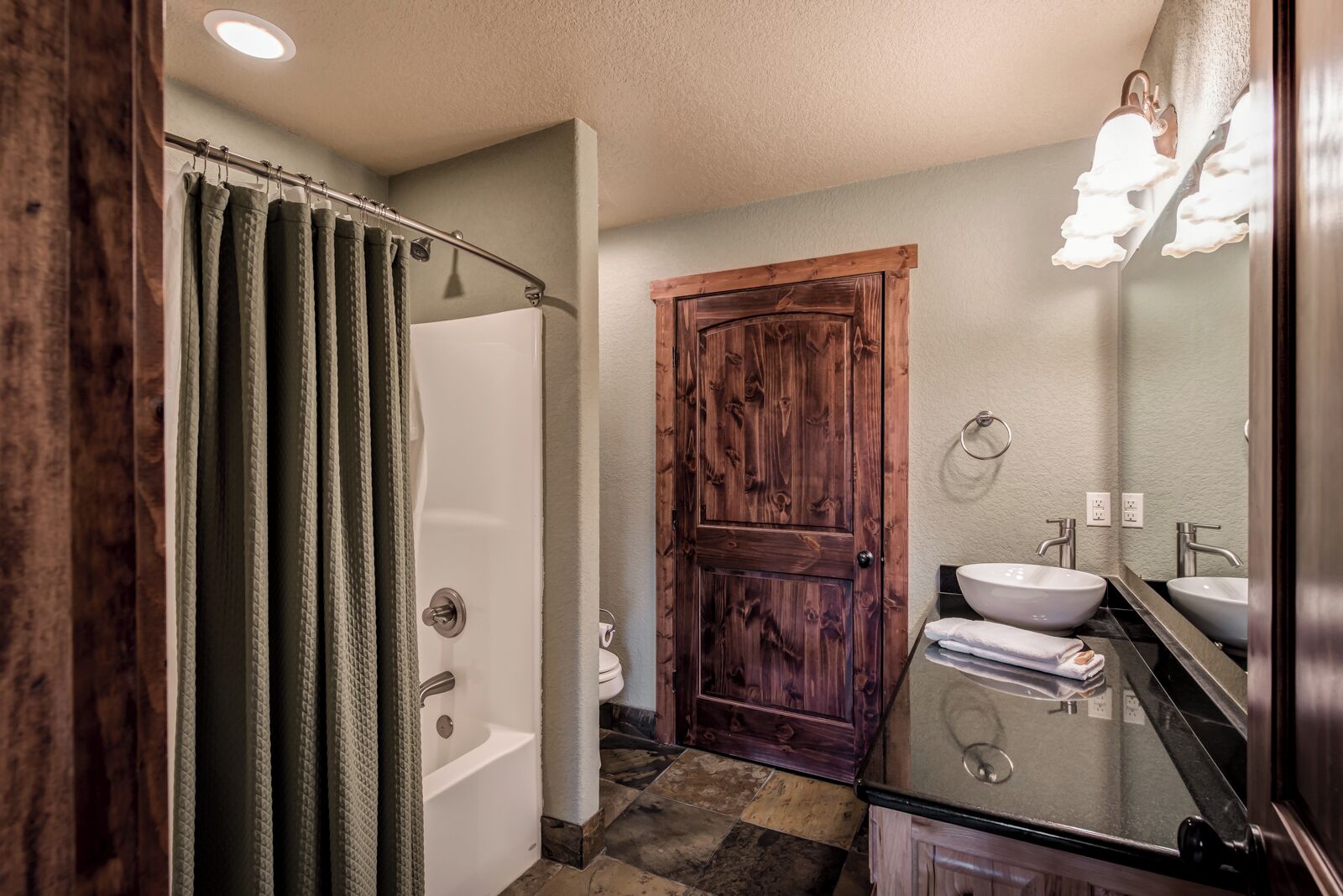 A bathroom with a bathtub, a wooden door, a sink, and a mirror.