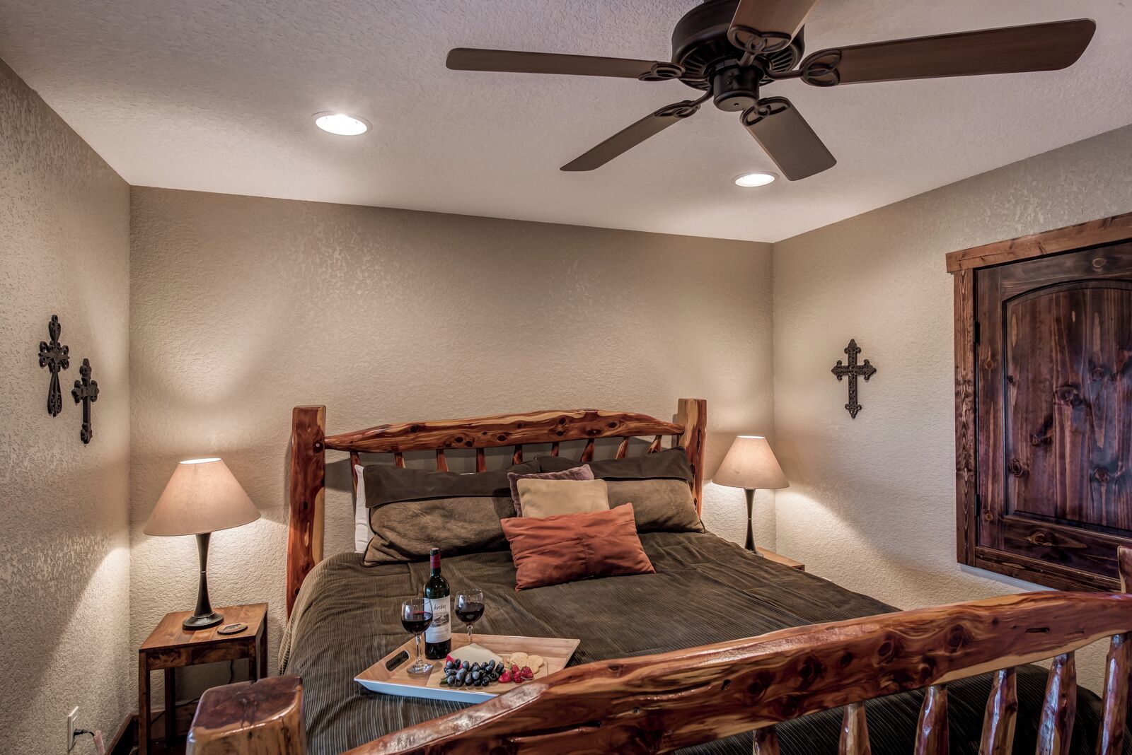 A bedroom with a wooden bed frame, two bedside lamps, a ceiling fan, and a wooden wardrobe.
