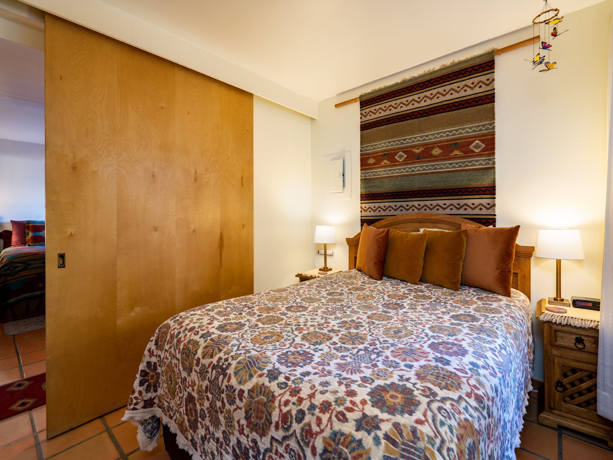 A bedroom with a large bed, a wooden door, a patterned rug, and a nightstand with a lamp.