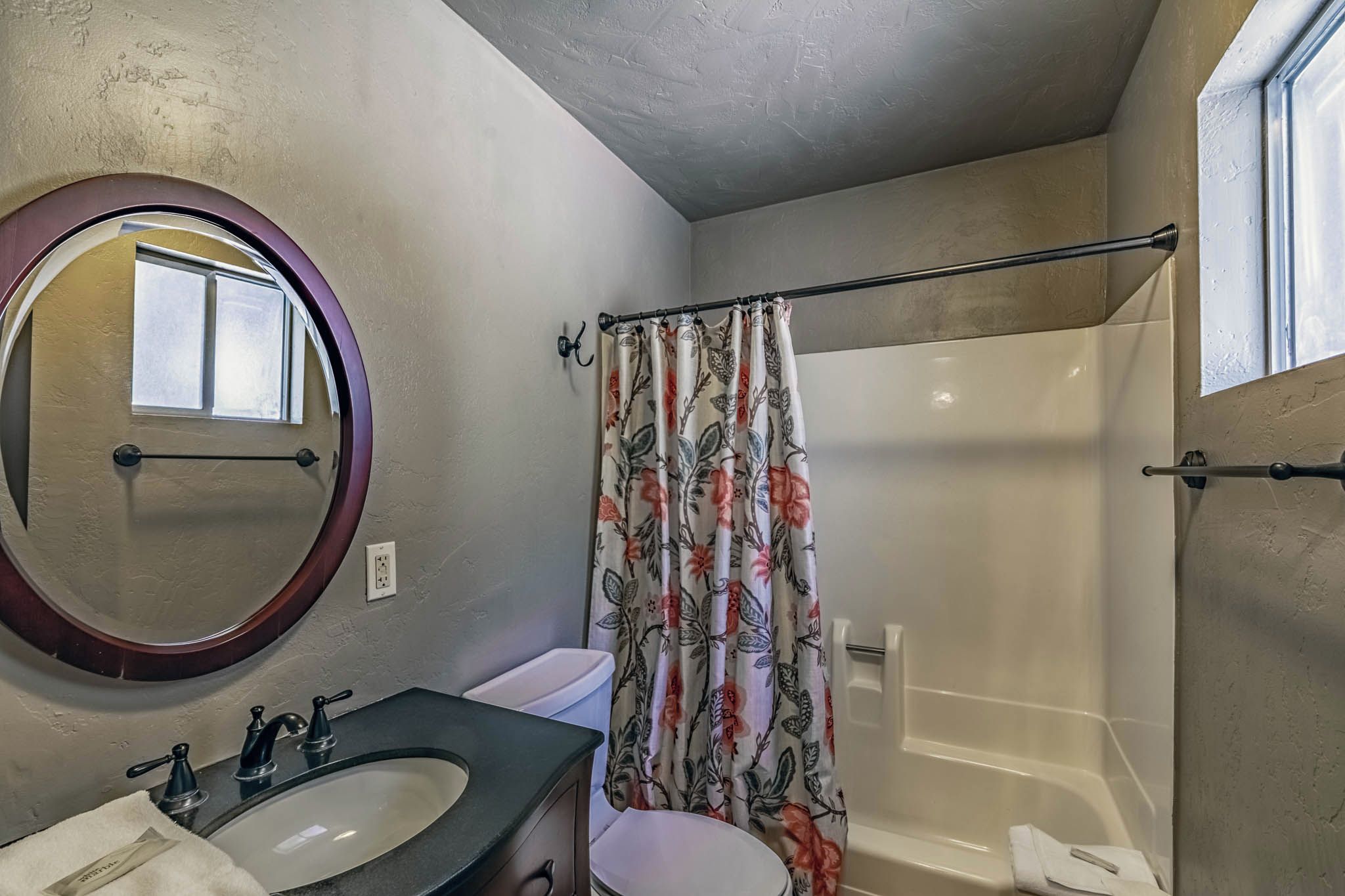 Un bagno con uno specchio rotondo, un lavabo, un WC e una zona doccia con tenda a fiori.