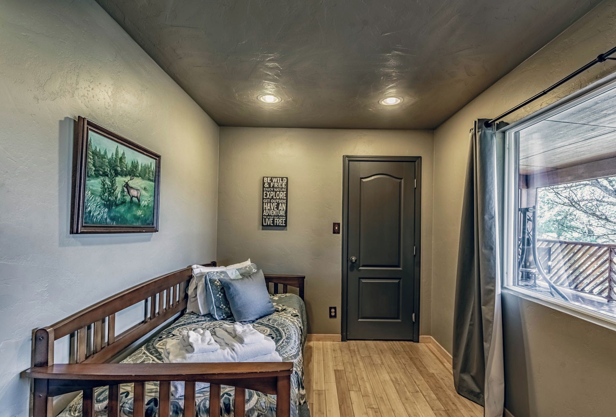 A bedroom with a bed, a framed picture, a motivational quote, a door, and a window.
