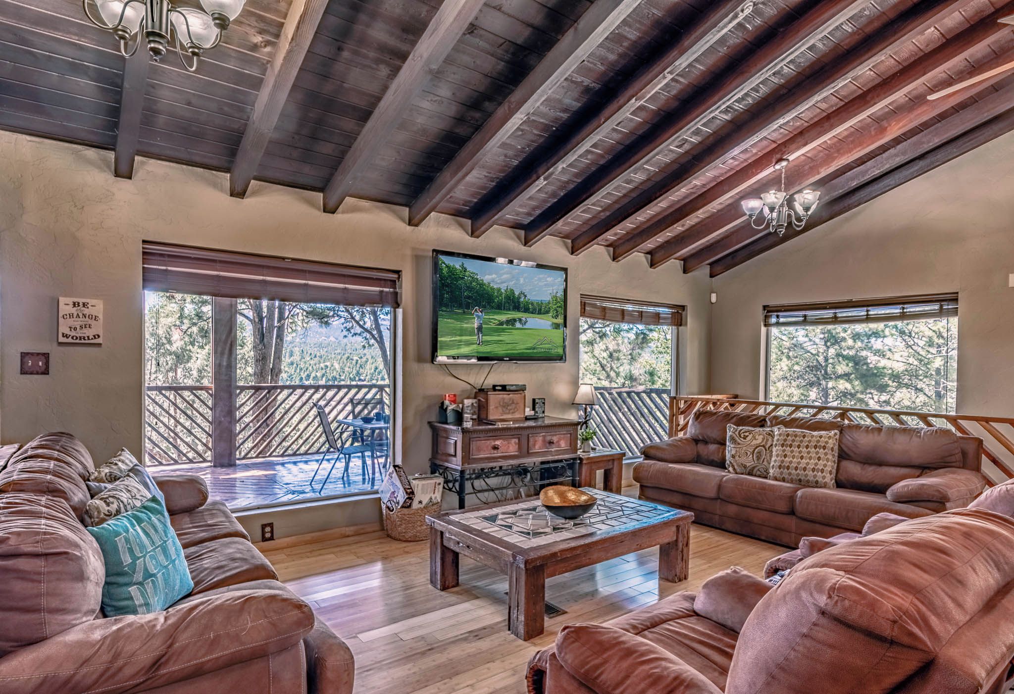 A spacious living room with a wooden ceiling, a large flat-screen TV mounted on the wall, and a comfortable seating area with sofas and a coffee table.