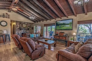 Ein geräumiges Wohnzimmer mit Ledersofas, einem Steinofen, einem großen Fernseher und einem Balkon mit Holzboden.