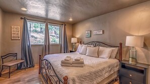 A bedroom with a bed, bedside tables, a chair, and a window with curtains. - Clearview by Ruidoso Vacation Rentals (Ruidoso)