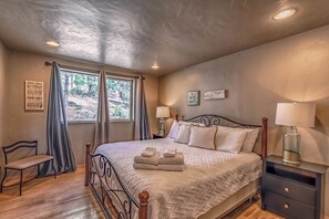 Quarto com cama, mesas de cabeceira, uma cadeira e janela com cortinas.