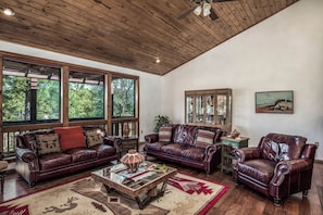 A spacious living room with leather sofas, a coffee table, and large windows offering a view of the outdoors. - Christi and Don's Nuthouse by Ruidoso Vacation Rentals (Ruidoso)