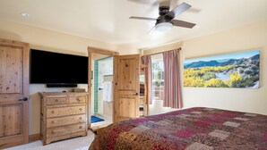 Un dormitorio con una cama grande, cómoda de madera, televisión y una vista panorámica de un río y montañas a través de una ventana.