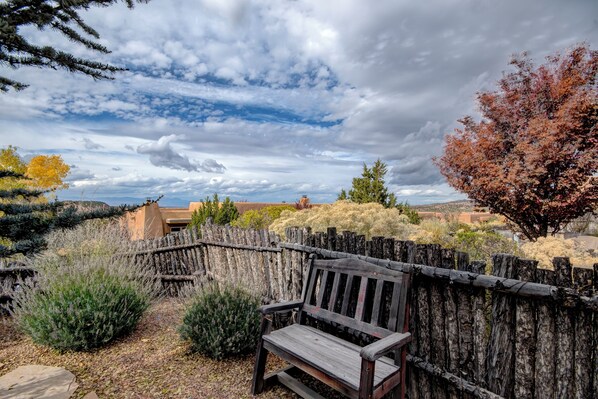 A wooden bench in a garden with a view of a distant building and a cloudy sky. - Cowboy Villa by Ruidoso Vacation Rentals (Santa Fe)