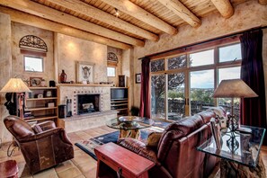 A cozy living room with a fireplace, leather sofas, and a large window offering a scenic view. - Cowboy Villa by Ruidoso Vacation Rentals (Santa Fe)