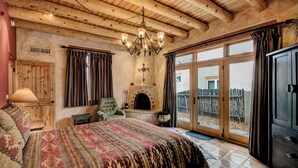 Camera da letto con un letto grande, soffitto in legno, camino e vista attraverso una porta vetrata.