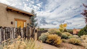 Un edificio rustico con una porta in legno, circondato da una recinzione di legno e diverse piante tipiche del deserto.