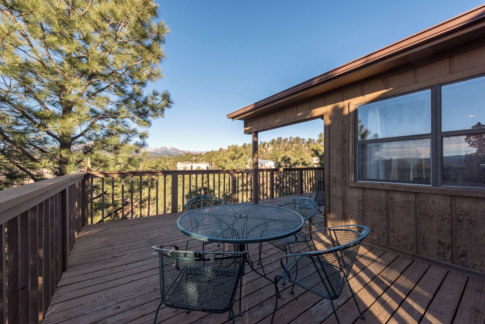 A wooden deck with a table and chairs, overlooking a mountainous landscape.