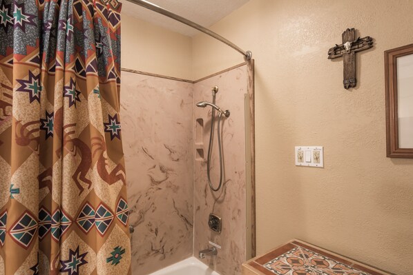 Een badkamer met een douche, wastafel, spiegel en een kruisbeeld aan de muur.
