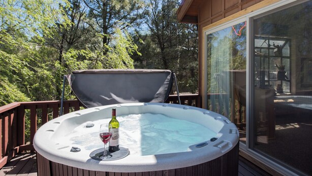 A hot tub on a wooden deck with a glass door leading to an outdoor area.