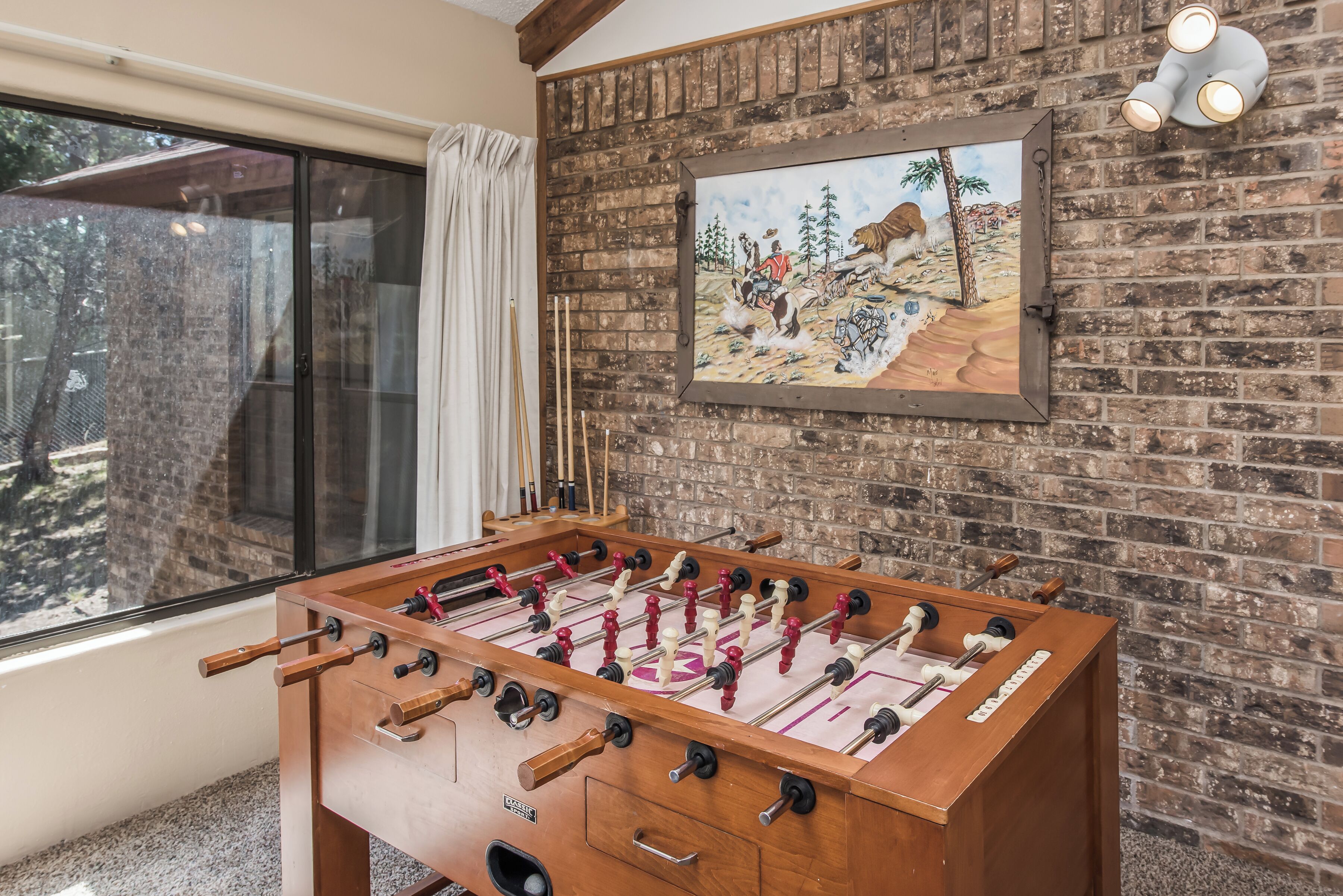 A foosball table in a room with a brick wall and a large window.