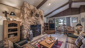 A cozy living room with a stone fireplace, wooden furniture, and a television.