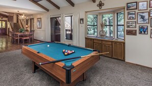 A pool table with a wooden frame and a green felt surface, surrounded by a carpeted floor and wooden cabinets.