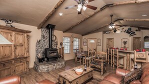 A rustic living room with a stone fireplace, wooden furniture, and a ceiling fan. - Cowboy Cabin by Ruidoso Vacation Rentals (Ruidoso)