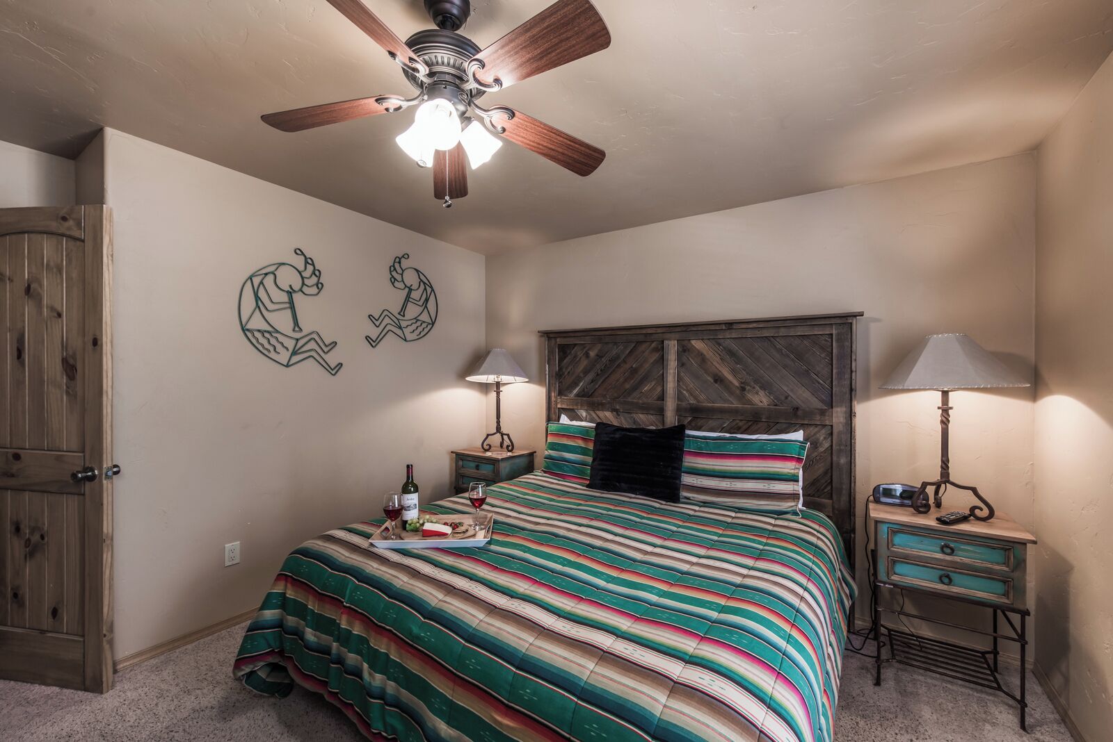 A bedroom with a bed, wooden headboard, two nightstands, a ceiling fan, and wall art.
