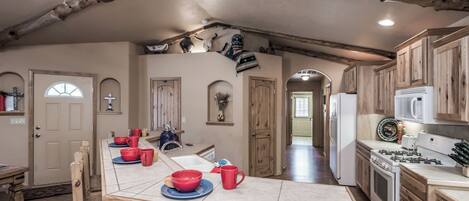 A rustic kitchen with wooden cabinets, a dining table with red cups, and a ceiling fan.