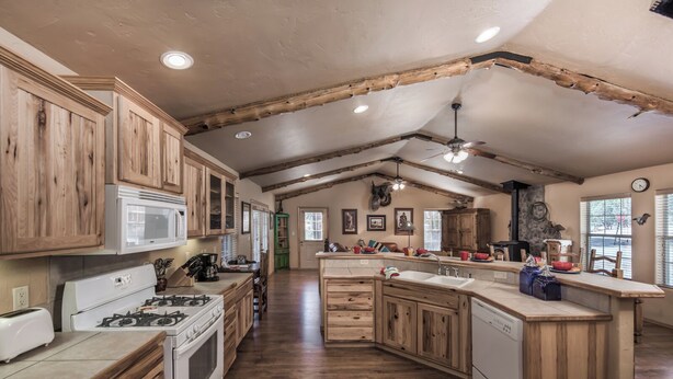 A spacious kitchen with wooden cabinets, a central island, and a dining area. - Cowboy Cabin by Ruidoso Vacation Rentals (Ruidoso)