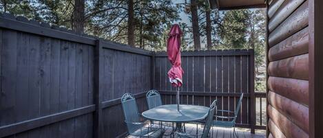 A wooden deck with a metal table and chairs, a red umbrella, and a wooden fence.