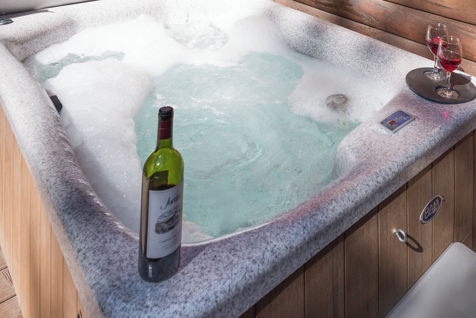 A hot tub with a bottle of wine and glasses on the edge.