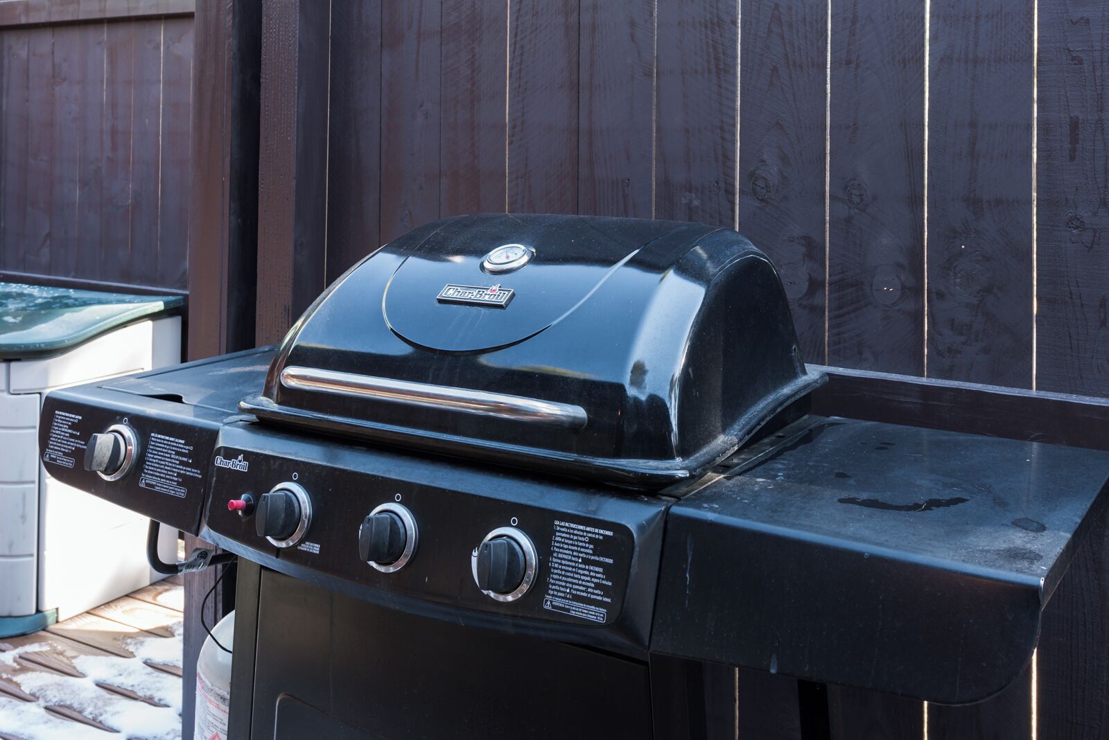 A Char-Broil gas grill with four burners and a side burner, set against a wooden fence.