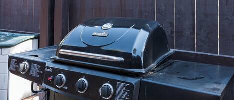 A Char-Broil gas grill with four burners and a side burner, set against a wooden fence.
