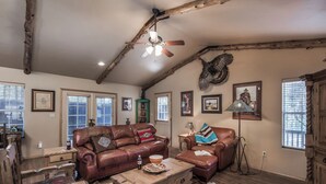 A rustic living room with a leather sofa, wooden coffee table, and a rustic fireplace. - Cowboy Cabin by Ruidoso Vacation Rentals (Ruidoso)