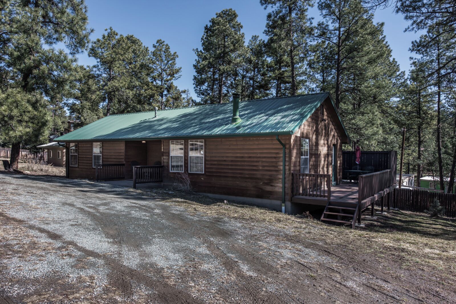 A rustic cabin with a green metal roof, wooden siding, and a porch.