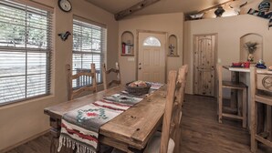 A dining area with a wooden table, chairs, and a window with blinds. - Cowboy Cabin by Ruidoso Vacation Rentals (Ruidoso)