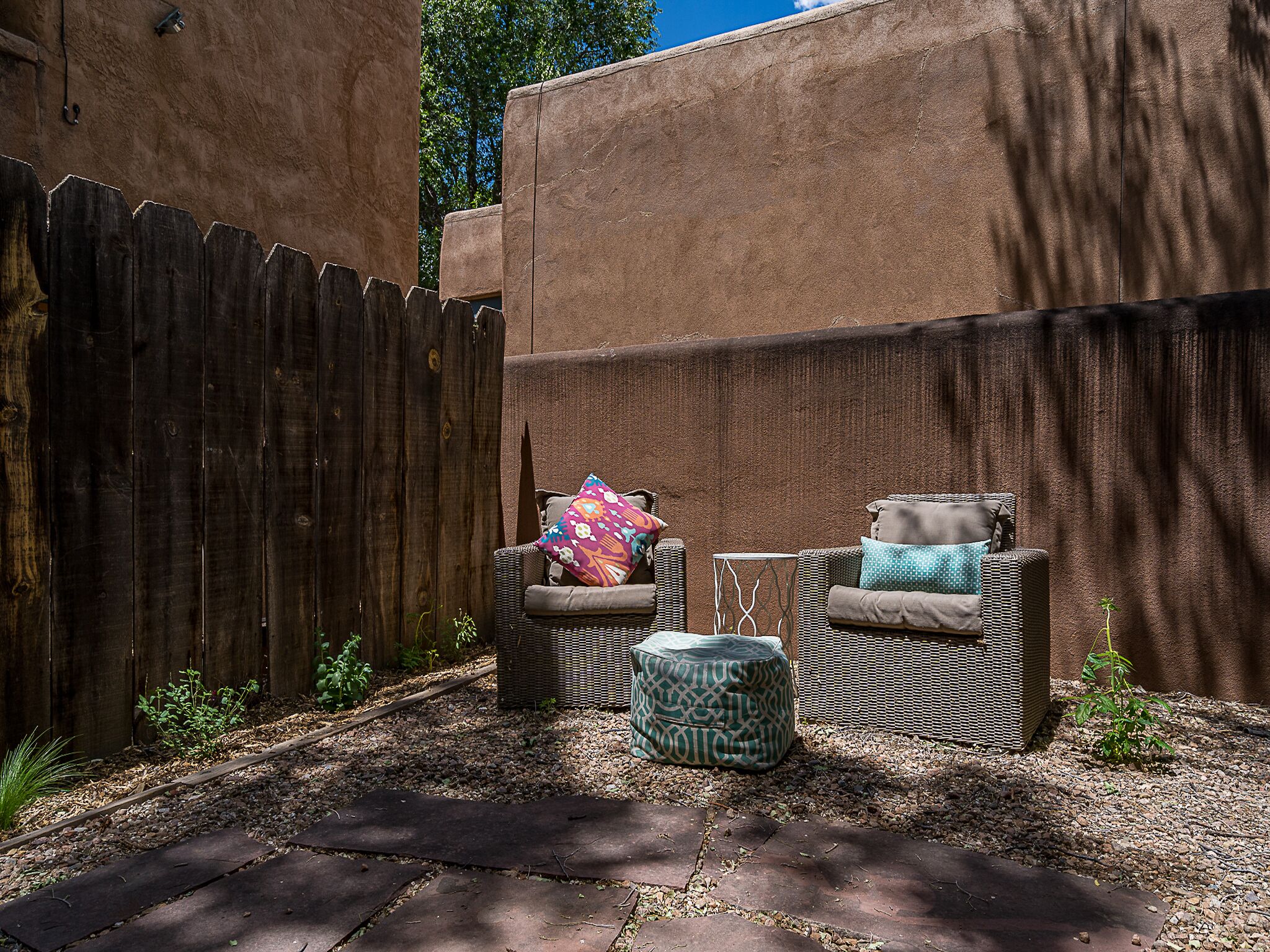 Un patio con dos sillas de mimbre y un reposapiés a juego, una cerca de madera y una pared con superficie texturizada.