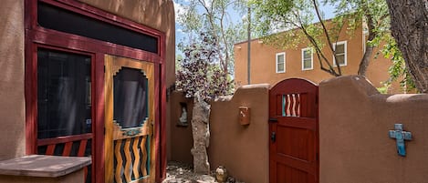 A narrow courtyard with a red door, a stone pathway, and a small statue.