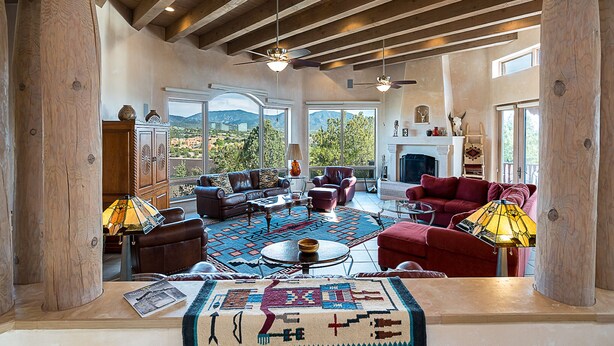 A spacious living room with a fireplace, leather sofas, and a large window offering a mountain view. - Dorthia Garden Retreat & Views by Kokopelli Property Management (Santa Fe)