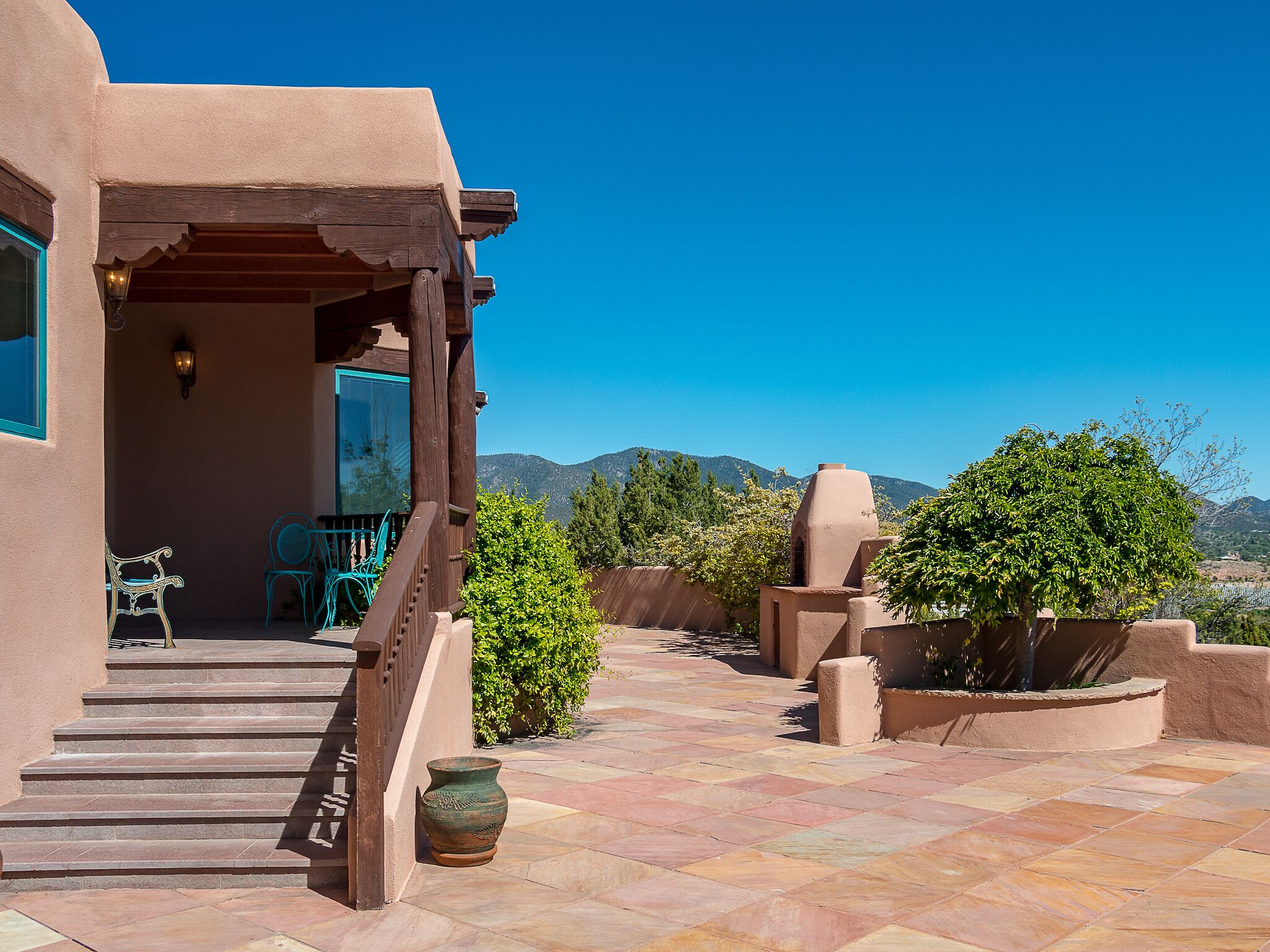 A patio with steps leading to a covered area, a wooden bench, and a potted plant.