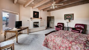 A bedroom with a bed, a television, a fireplace, and leather chairs. - Dorthia Garden Retreat & Views by Kokopelli Property Management (Santa Fe)