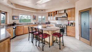 A spacious kitchen with wooden cabinets, a central island with bar stools, a built-in oven, and a large window providing natural light. - Dorthia Garden Retreat & Views by Kokopelli Property Management (Santa Fe)