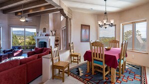 A spacious living area with a fireplace, a dining table with chairs, and a large window offering a view of the outdoors. - Dorthia Garden Retreat & Views by Kokopelli Property Management (Santa Fe)