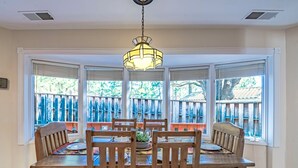 A dining area with a wooden table and chairs, large windows with blinds, and a hanging light fixture. - DB Mountain by Ruidoso Vacation Rentals (Ruidoso)